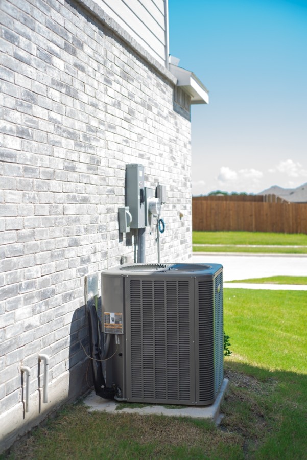 An outdoor air conditioning unit next to a brick wall on a sunny day.